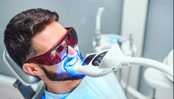 man sitting in a dentist office getting a teeth whitening procedure done